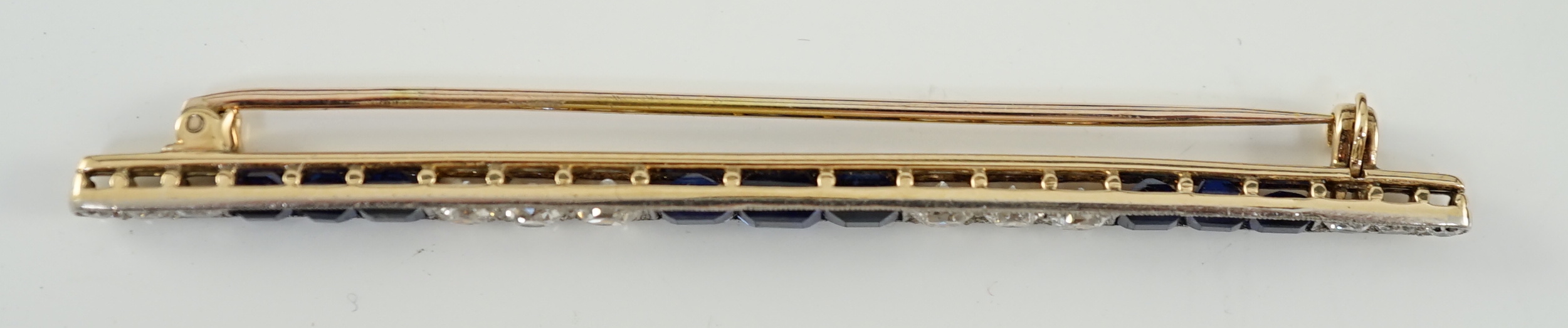 An Art Deco, round cut diamond and rectangular cut sapphire cluster bar brooch